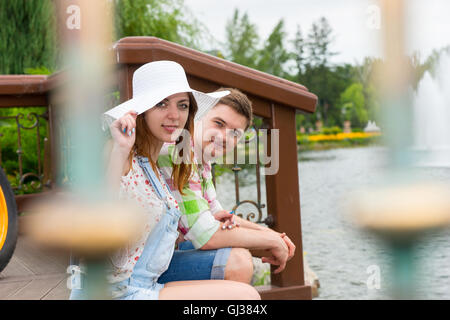 Junge romantisch zu zweit sitzen auf dem Holzdeck gegenüber dem künstlichen See in einem Park mit Brunnen und verschiedene Bäume in einer b Stockfoto