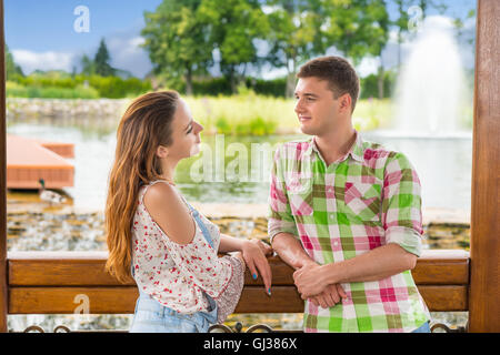 Romantische Pärchen stützte sich auf Geländer von der Holzpavillon und sahen einander vor menschengemachten Wasserfall in einem Park mit Teich, Brunnen und verschiedene Bäume stehen. Stockfoto