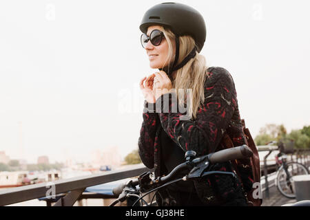 Junge Frau im Freien, auf Helm, bereit, mit dem Fahrrad Stockfoto