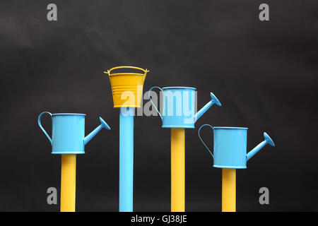 Paar Gießkannen und einen Eimer in einer Reihe auf dunklem Hintergrund Stockfoto