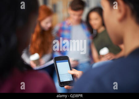 Junge männliche und weibliche Studenten lesen Smartphone Texte im Aufenthaltsraum Stockfoto