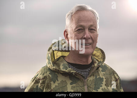 Mann mit Blick in die Kamera wasserdicht mit Kapuze Camouflage-Mantel Stockfoto