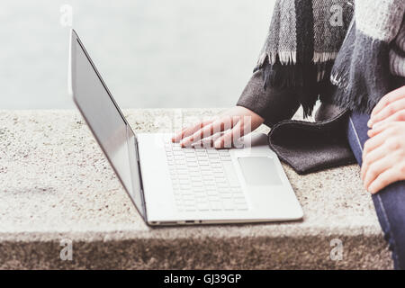 Beschnitten, Aufnahme des jungen Paares mit Laptop auf der Hafenmauer, Comer See, Italien Stockfoto