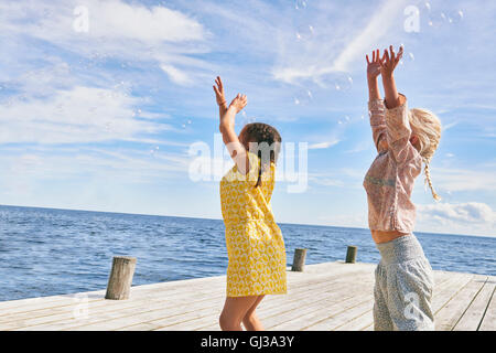 Zwei junge Freunde spielen auf hölzerne Pier erreichen Blasen Stockfoto