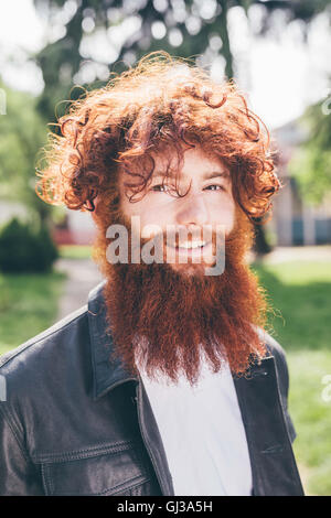 Porträt des jungen männlichen Hipster mit lockigen roten Haaren und Bart im park Stockfoto