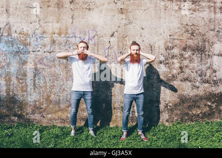 Porträt des jungen männlichen Hipster Zwillinge mit roten Bärte stehen vor der Wand mit Händen, Mund und Ohren abdecken Stockfoto