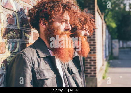 Junge männliche Hipster Zwillinge mit roten Haaren und Bärten Ziegelwand gelehnt Stockfoto