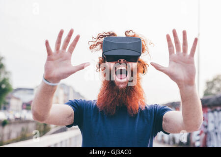 Porträt des jungen männlichen Hipster mit roten Haaren und Bart schreien während virtual-Reality-Kopfhörer tragen Stockfoto