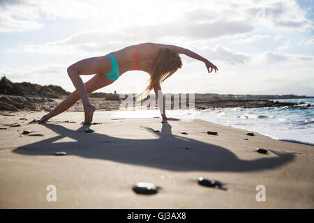 Junge Frau am Strand, in Yogaposition, Rückansicht Stockfoto