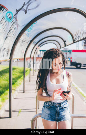 Junge Frau mit Dreadlocks mit Smartphone Touchscreen in städtische Wartehäuschen Stockfoto