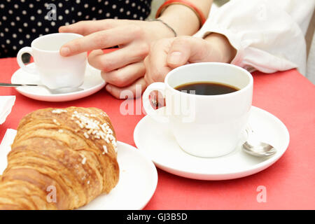 Nahaufnahme von Frauenhand mit schwarzen Kaffee und Croissants am Straßencafé Stockfoto