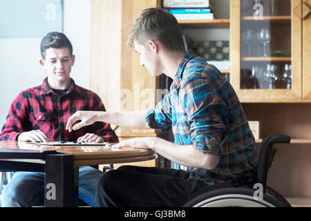 Junger Mann mit Rollstuhl spielen Zugluft mit Freund in Küche Stockfoto