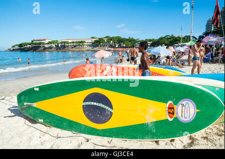 RIO DE JANEIRO - 5. April 2016: Brasilien Fahne stand Paddel Surfbrett Wartezeiten für Kunden am Strand der Copacabana. Stockfoto