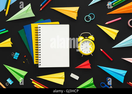 Multicolor Notebooks mit Papier, Origami Flugzeuge und Wecker auf dem schwarzen Hintergrund. Zurück zum Schulkonzept mit Textfreiraum. Stockfoto