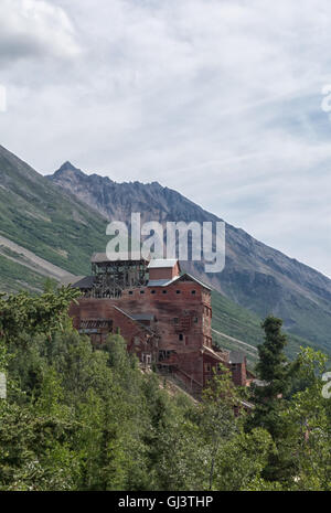 Das verblasste rote Mühle-Haus der Kennicott Mine steht Shorouded von einem Wald mit einem Berg im Hintergrund. Stockfoto