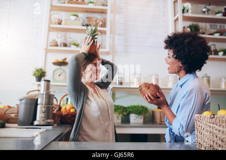 Saft-Bar-Mitarbeiter spielen mit Früchten am Arbeitsplatz. Junge Frauen halten, Kokosnuss und Ananas im stehen am Tresen. Stockfoto