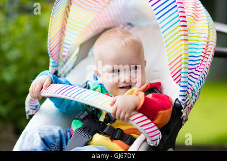 Baby Junge im weißen Pullover sitzen in weißen Kinderwagen auf einen Spaziergang in einem Park. Kind im regenbogenfarbenen Buggy. Stockfoto