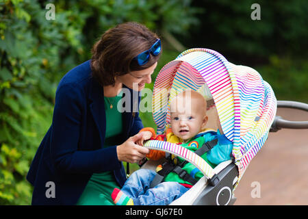 Junge Berufstätige Mutter und formale Büro-Outfit zu Fuß mit ihrem Baby in bunte Kinderwagen. Mutter und Kind im Kinderwagen. Stockfoto