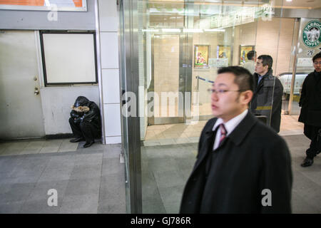 Obdachlosen Kerl, Mann, Schlafen, Mangel an, Schlaf, beraubt, an einem kalten Wintertag im Januar am Eingang/Ausgang Ost von Shinjuku, Tokyo. Japan. Stockfoto