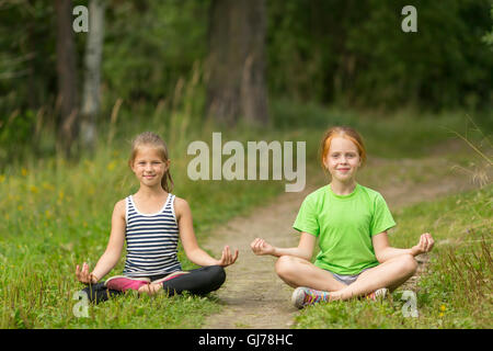 Zwei kleine süße Mädchen sitzen im Lotussitz in den Park. Yoga und eine gesunde Lebensweise. Stockfoto