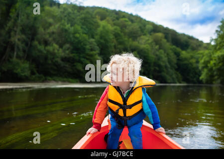 Glückliches Kind genießen Kajakfahrt auf schönen Fluss. Kleinen lockigen Kleinkind Jungen Kajak an heißen Sommertag. Wassersport und camping Stockfoto