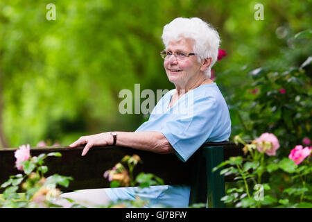 Glücklich senior Behinderte Dame mit einer Gehbehinderung, genießen Sie einen Spaziergang in einem sonnigen Park schieben ihre Gehhilfe oder Rollstuhl, Stockfoto