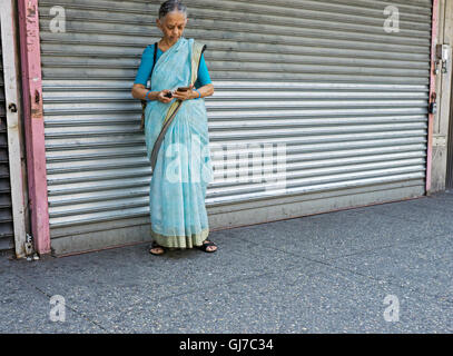 Eine indische Frau auf der 82nd Street in Jackson Heights Queens, New York tragen traditionelle Kleidung und Lesen von e-Mails auf dem Handy Stockfoto