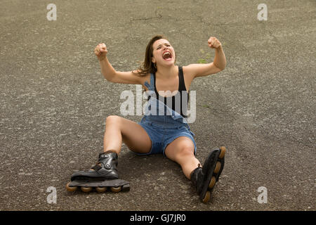 junge Frau mit Inline-Skates sitzen auf Asphalt und schreien Stockfoto