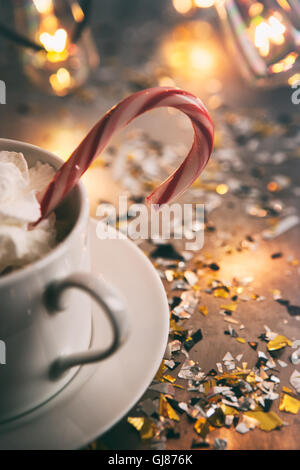 Urlaub: Zuckerstange In Tasse Kakao mit Glühbirnen hinter Stockfoto