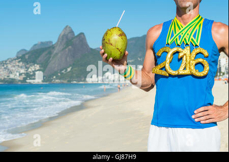 Goldmedaille 2016 Sportler halten frische Coco Gelado grüne Kokosnuss am Strand von Ipanema in Rio De Janeiro, Brasilien Stockfoto