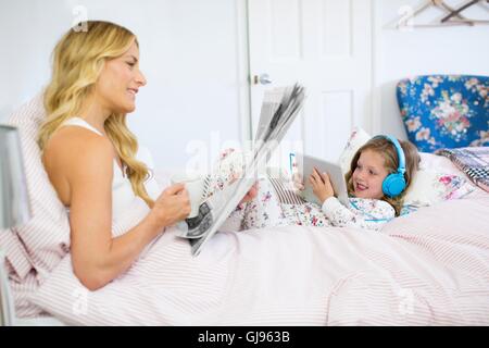EIGENTUM FREIGEGEBEN. -MODELL VERÖFFENTLICHT. Mutter und Tochter im Bett mit Zeitung und digital-Tablette. Stockfoto