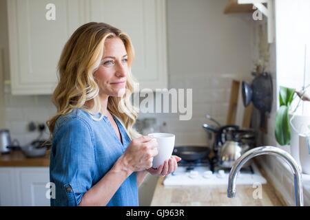 EIGENTUM FREIGEGEBEN. -MODELL VERÖFFENTLICHT. Frau in der Küche mit Heißgetränk, Porträt. Stockfoto