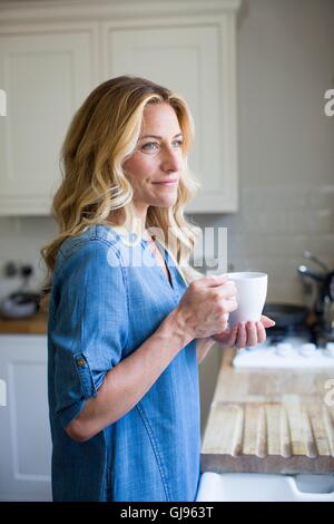 EIGENTUM FREIGEGEBEN. -MODELL VERÖFFENTLICHT. Frau in der Küche mit Heißgetränk, Porträt. Stockfoto