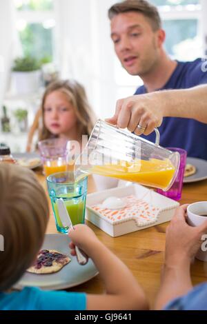 EIGENTUM FREIGEGEBEN. -MODELL VERÖFFENTLICHT. Vater aus einem Krug gießen Orangensaft beim Frühstück. Stockfoto