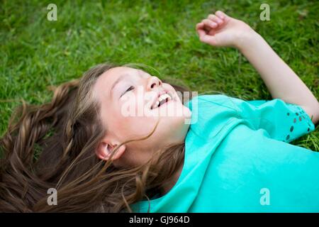 EIGENTUM FREIGEGEBEN. -MODELL VERÖFFENTLICHT. Junges Mädchen auf dem Rasen liegend Lächeln auf den Lippen. Stockfoto