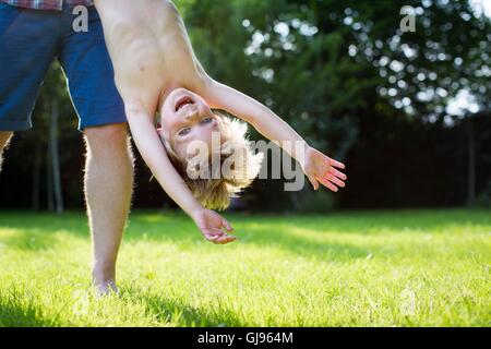 EIGENTUM FREIGEGEBEN. -MODELL VERÖFFENTLICHT. Vater Holding Sohn kopfüber in den Garten. Stockfoto