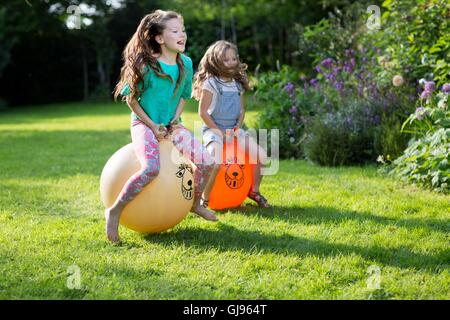 EIGENTUM FREIGEGEBEN. -MODELL VERÖFFENTLICHT. Zwei Schwestern Prellen auf bouncy Trichter im Garten. Stockfoto