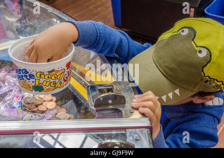 Ein kleiner Junge spielt auf einem 2P-Spielautomaten in einer Spielhalle in einem Ferienort. Stockfoto