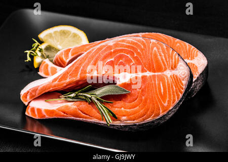 Zwei Scheiben Lachs Steak mit Zitrone und Kräutern auf schwarz Stockfoto