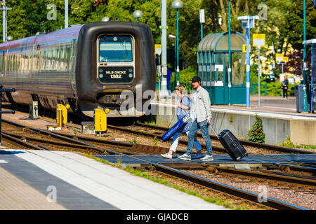 Kalmar, Schweden - 10. August 2016: Menschen mit Trolley-Taschen über die Gleise am Bahnhof kommt man zu der Plattform. Stockfoto