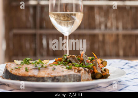 Gebackener Thunfisch Steak mit gedünsteten Okra auf dem weißen Teller garnieren diente für ein Abendessen mit einem Glas weißen Wein Closeup. Stockfoto