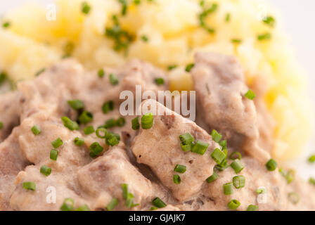 Boeuf Stroganoff mit Kartoffelpüree mit Frühlingszwiebeln auf der weißen Platte Nahaufnahme verziert. Stockfoto