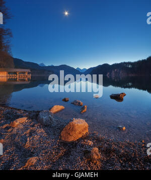 Übernachtung in Alpsee See Deutschlands. Wunderschöne Landschaft mit See, Berge, Wald, Sterne, Vollmond, blauer Himmel und Steinen Stockfoto