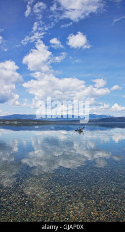 Person Kajak durch Wolke Reflexionen auf ruhigem Wasser in Atlin Lake, Yukon-Territorium im Sommer. Stockfoto