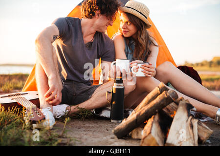 Zugeschnittenes Bild eines jungen Paares, das Trinken von Tee am Lagerfeuer beim camping Stockfoto