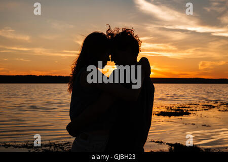 Zwei jungen Liebenden stehen am Strand und sahen einander auf Sonnenuntergang Hintergrund Stockfoto