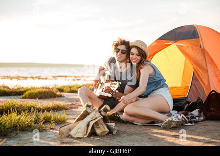 Glückliches junges Paar spielen Gitarre und Braten Marshmallows am Lagerfeuer zusammen Stockfoto