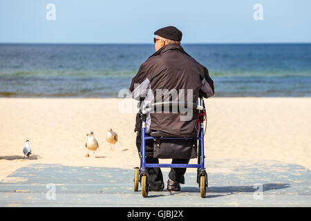 KOLOBRZEG, Polen - 7. April 2016: Behinderte ältere Menschen in einem Rollstuhl sitzt und blickt auf das Meer Stockfoto