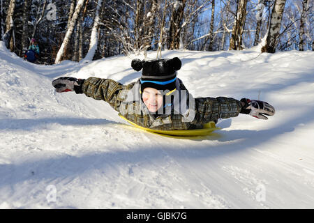 Kleiner Junge reitet mit Hügeln auf dem Schlitten im Winterwetter Stockfoto