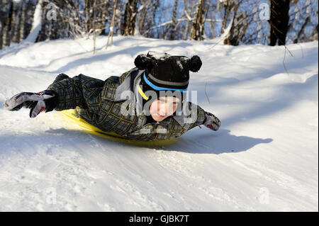 Kleiner Junge reitet mit Hügeln auf dem Schlitten im Winterwetter Stockfoto